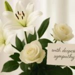 White lilies and roses with a sympathy card showing funeral flower message ideas.